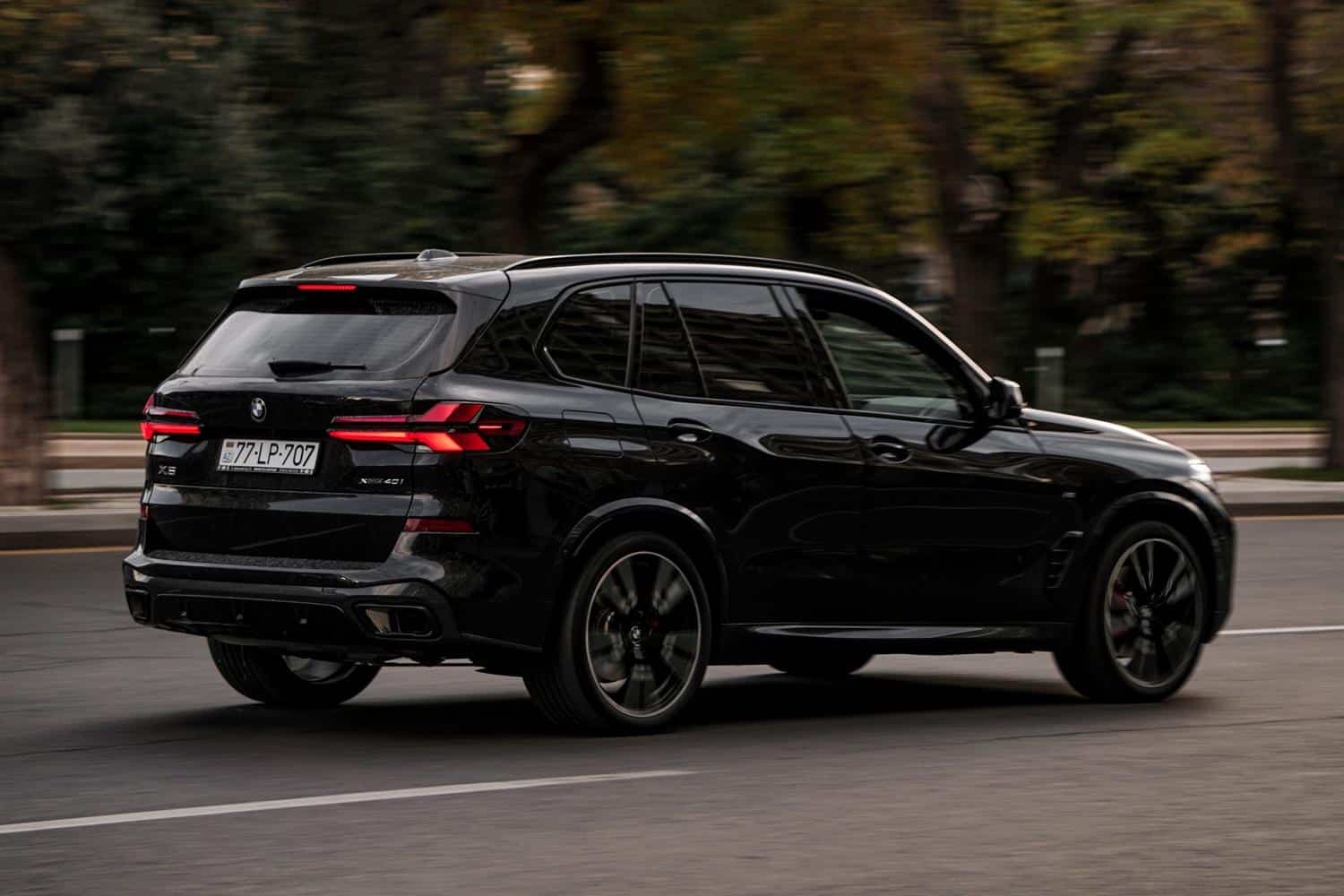 BMW X5 negro circulando por calles urbanas en un día soleado, representando la versatilidad y el lujo en la ciudad.