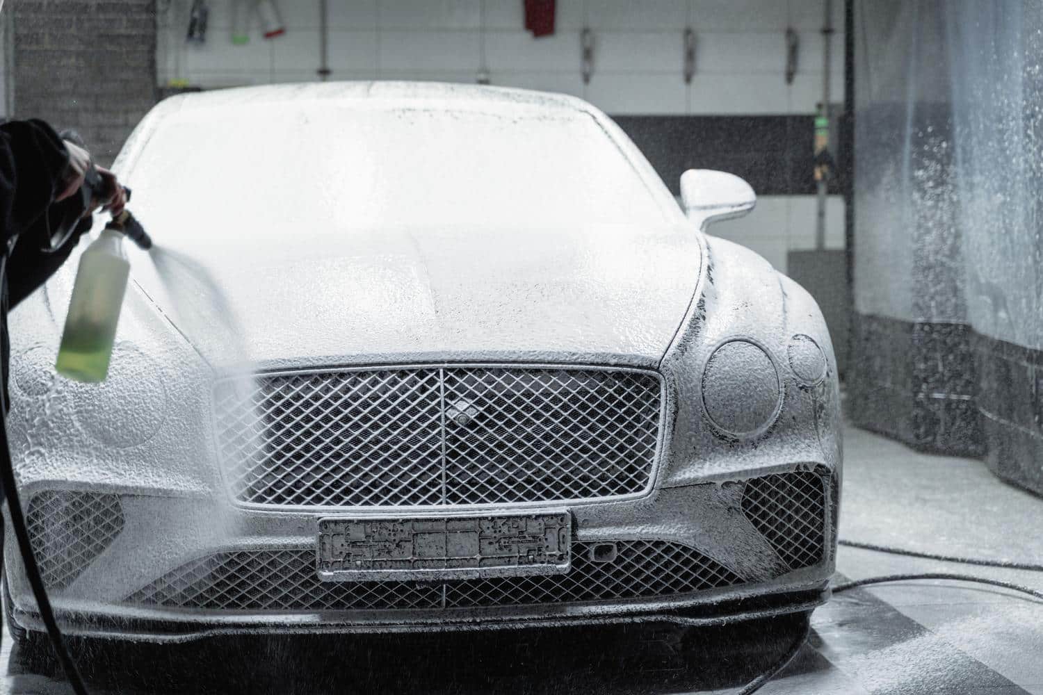Coche de lujo cubierto de espuma activa durante un prelavado de detailing para evitar microarañazos.