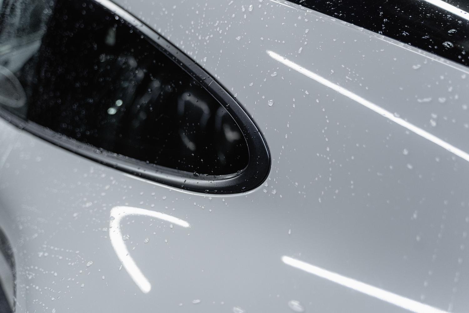 Primer plano de gotas de agua sobre la carrocería de un coche blanco, demostrando el efecto hidrofóbico de un sellado cerámico.