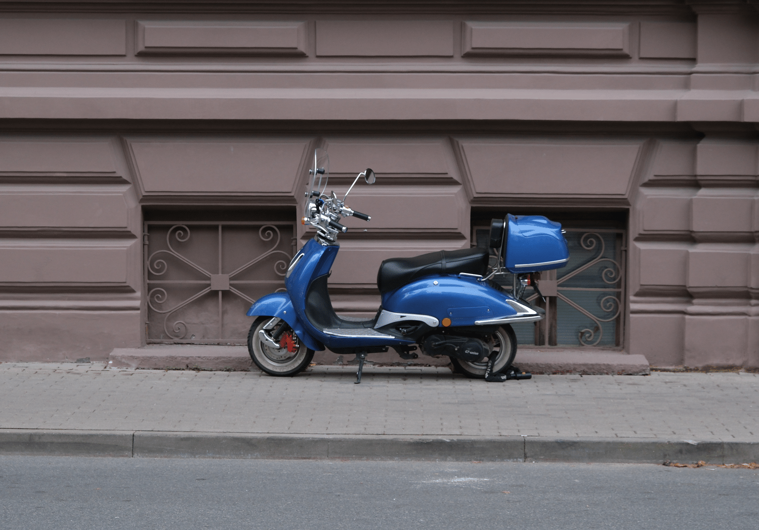 Ciclomotor eléctrico azul aparcado en una calle histórica, destacando la capacidad de circular por centros urbanos y Zonas de Bajas Emisiones.
