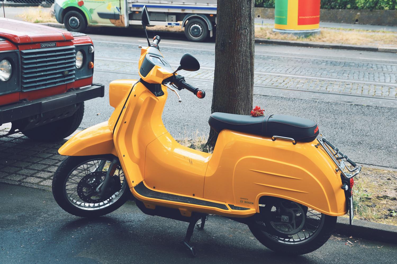 Scooter eléctrico amarillo brillante en una calle de la ciudad, ideal para desplazamientos urbanos ágiles.