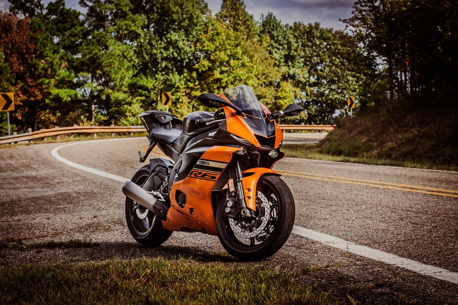 Motocicleta aparcada en una carretera curva rodeada de árboles otoñales, reflejando la tranquilidad del entorno.