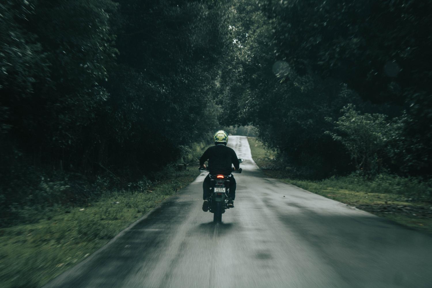 Un motociclista solitario recorriendo una carretera rural serena bordeada de árboles, evocando paz mental.