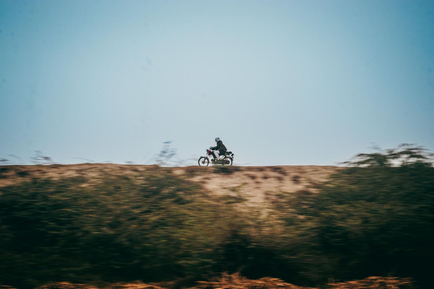 Motociclista conduciendo por un paisaje abierto bajo un cielo azul despejado, transmitiendo libertad y aventura.