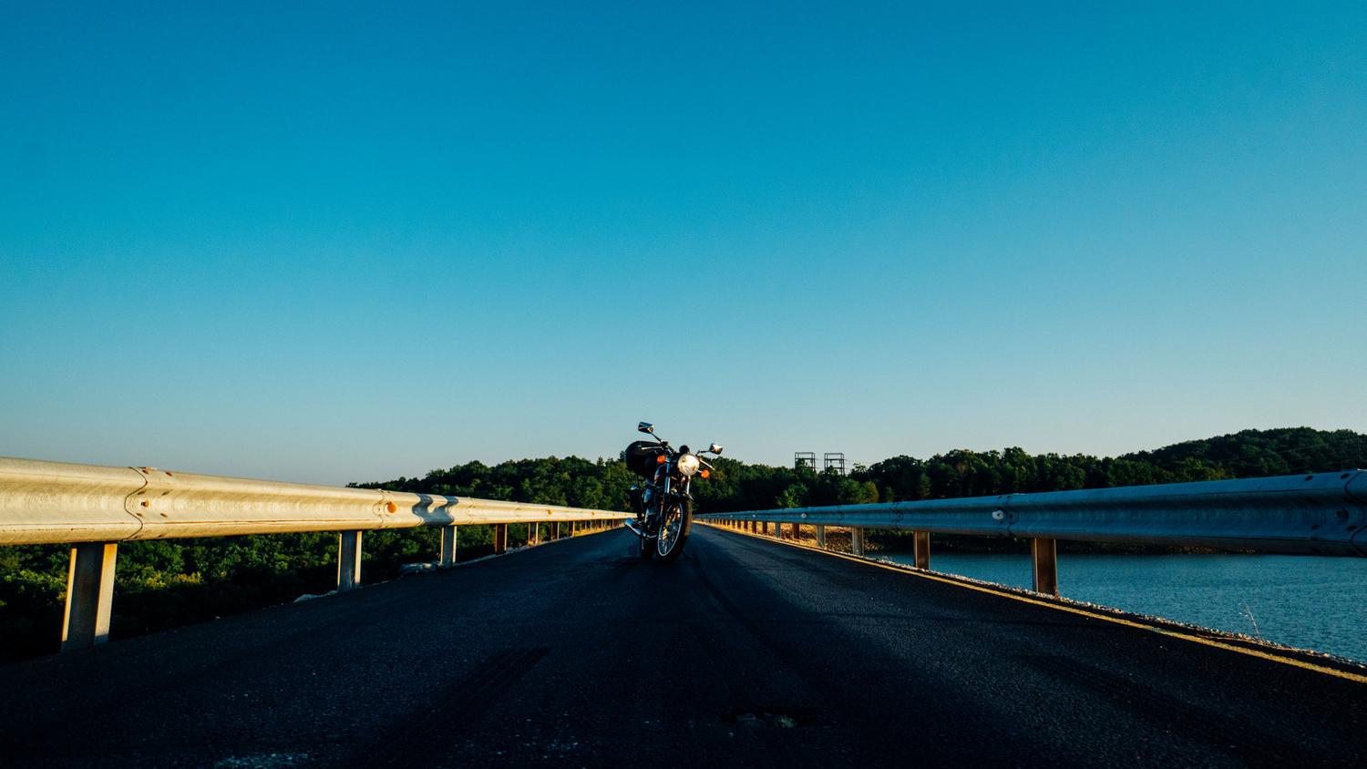Motocicleta cruzando un puente escénico durante el atardecer, simbolizando la evasión del estrés diario.