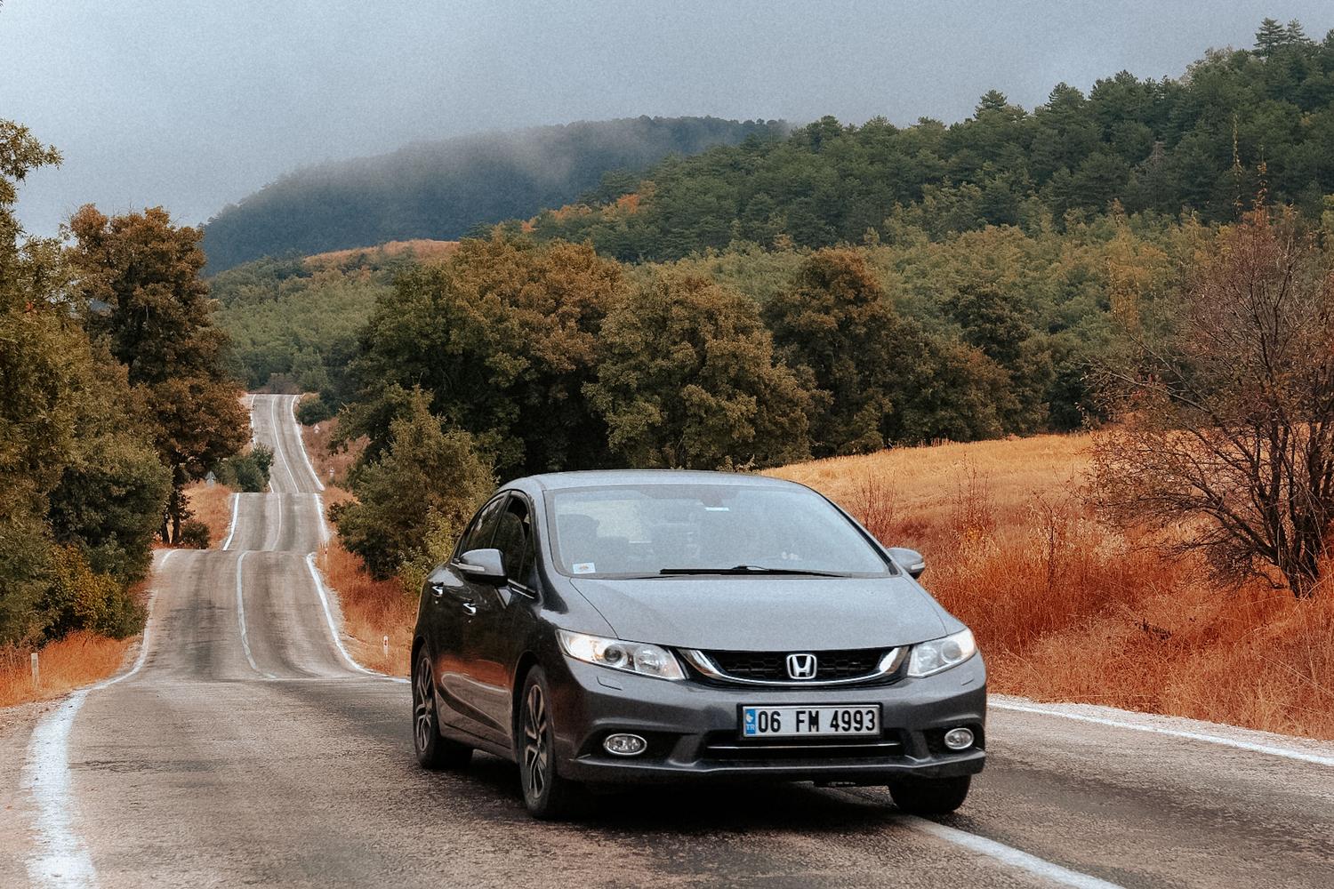 Coche moderno circulando por una carretera escénica rodeada de naturaleza y colores otoñales.