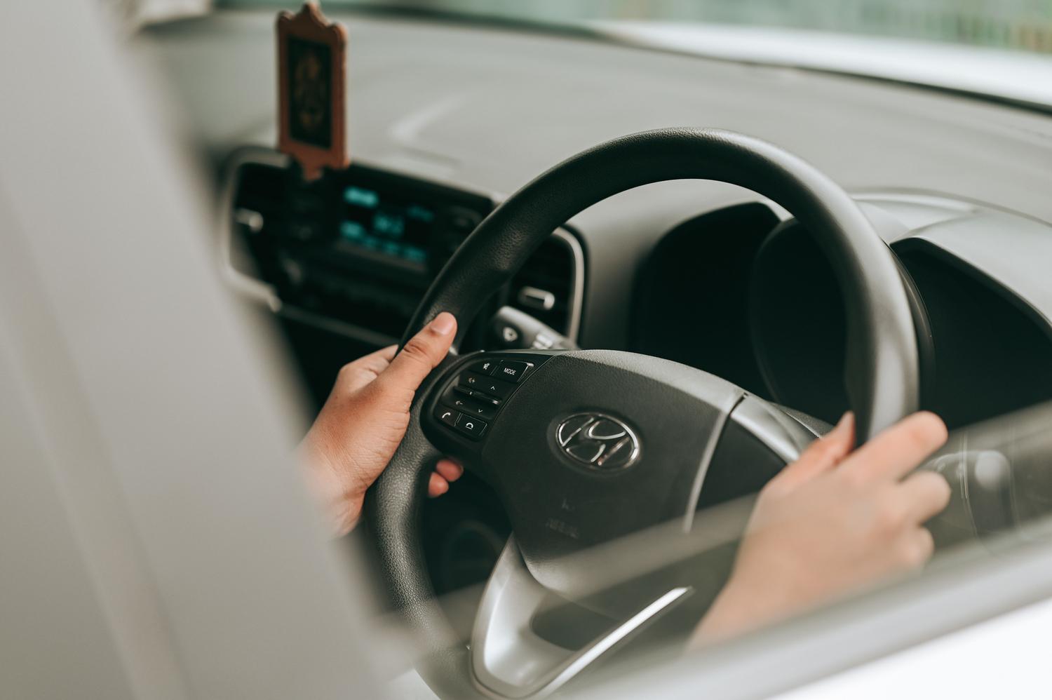 Primer plano de las manos de un conductor sujetando correctamente el volante de un coche moderno.