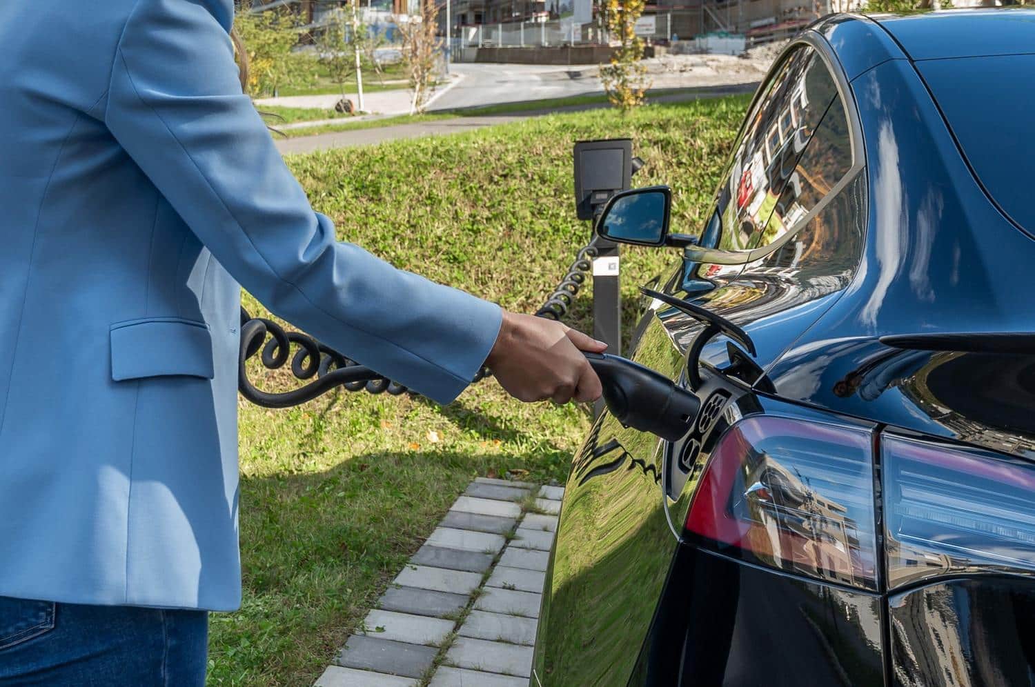Persona conectando el cable de carga a un coche eléctrico en un entorno urbano, mostrando el proceso de carga diaria.