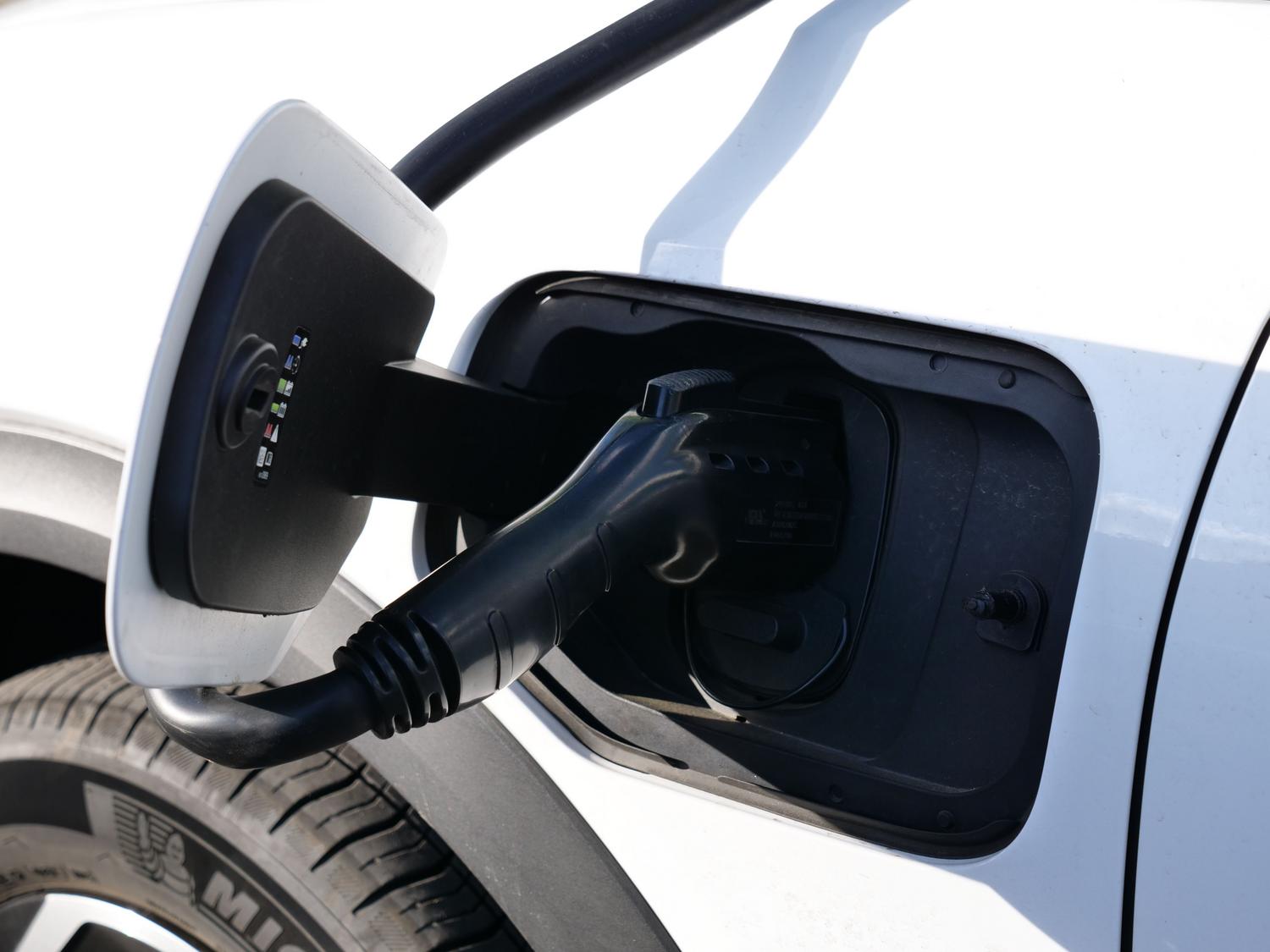 Primer plano de un conector de carga de un vehículo eléctrico insertado en el puerto de carga, ilustrando la tecnología de electrificación.