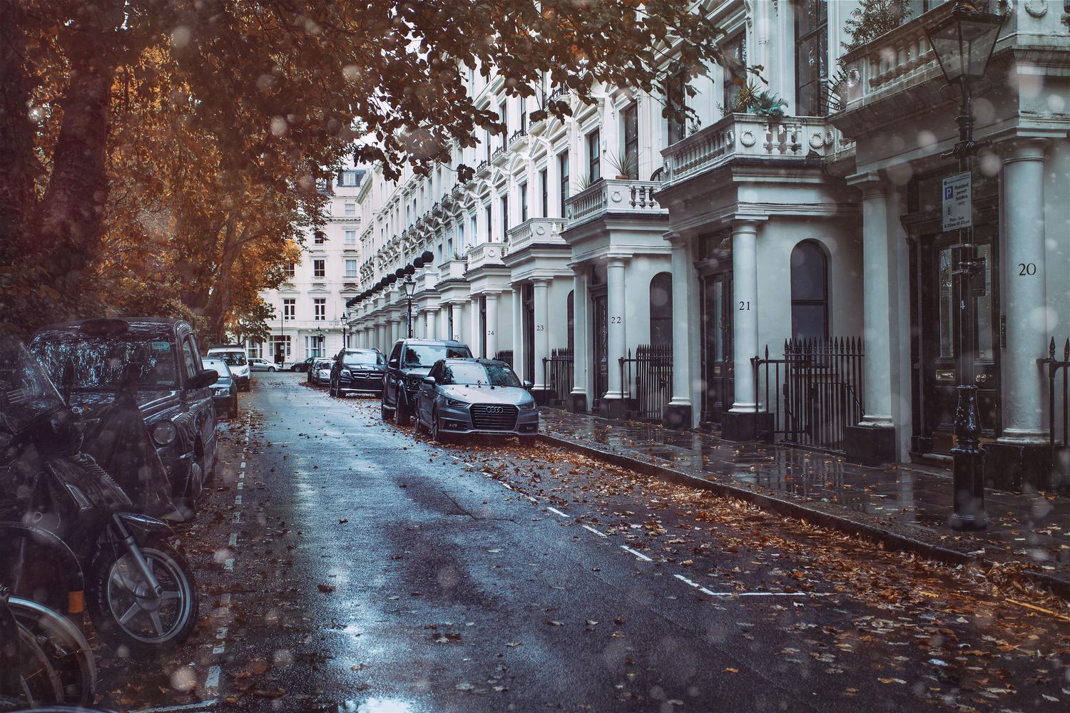Vehículos estacionados en paralelo en una estrecha calle de Londres bajo la lluvia.