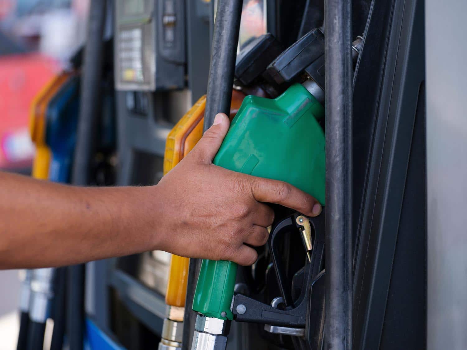 Primer plano de una mano sosteniendo una boquilla de combustible de color verde en una estación de servicio, simbolizando el uso de combustibles renovables.