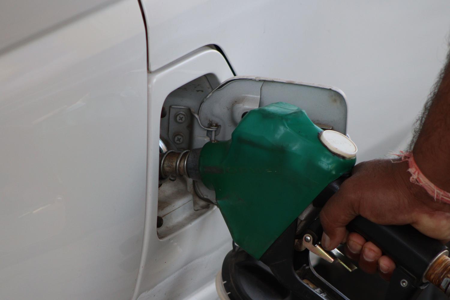 Persona repostando un vehículo en una gasolinera utilizando una boquilla de color verde, representando la transición a combustibles sostenibles.