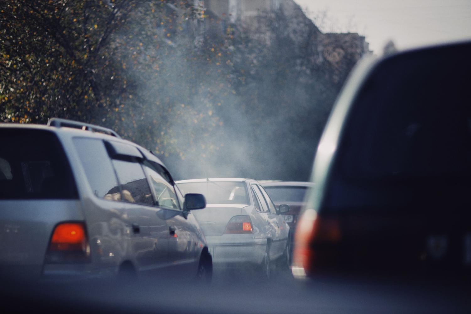 Atasco de tráfico en una ciudad con vehículos emitiendo gases contaminantes, representando la polución urbana.